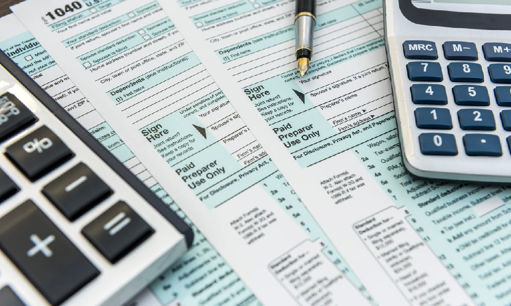Tax forms sit on a table with pen and calculators as someone prepares to fill out form 8965.