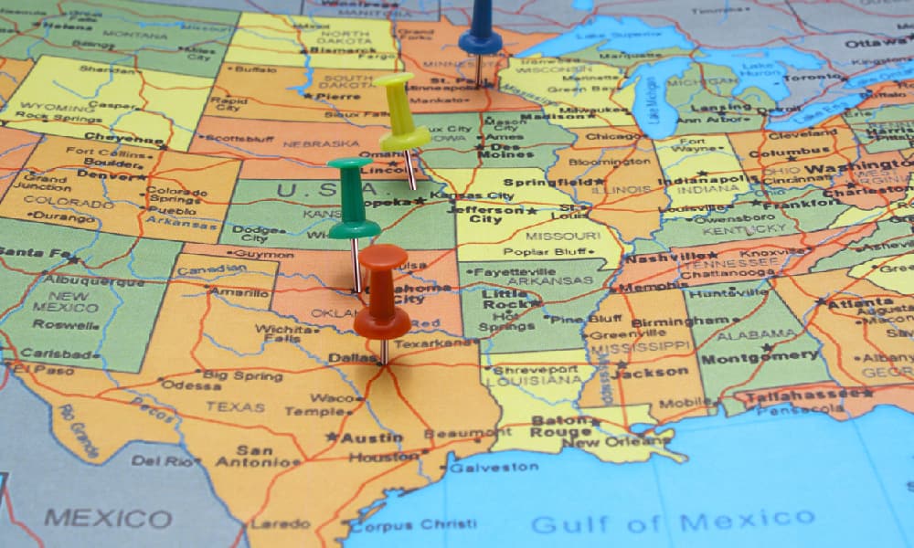 Four pins showing on a colorful map of the United States illustrate someone needing to pay multiple state tax returns.