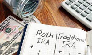 roth IRA and traditional IRA written in a notebook next to fifty dollar bills and a calculator on a desk, illustrating our guide to IRS form 8880 and the Saver’s Credit