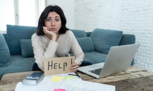 Frustrated woman sitting on a couch with a help sign as she deals with a failure to pay penalty