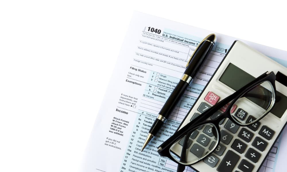 A tax form, pair of glasses, pen, and calculator on a white background, representing the scope of an audit