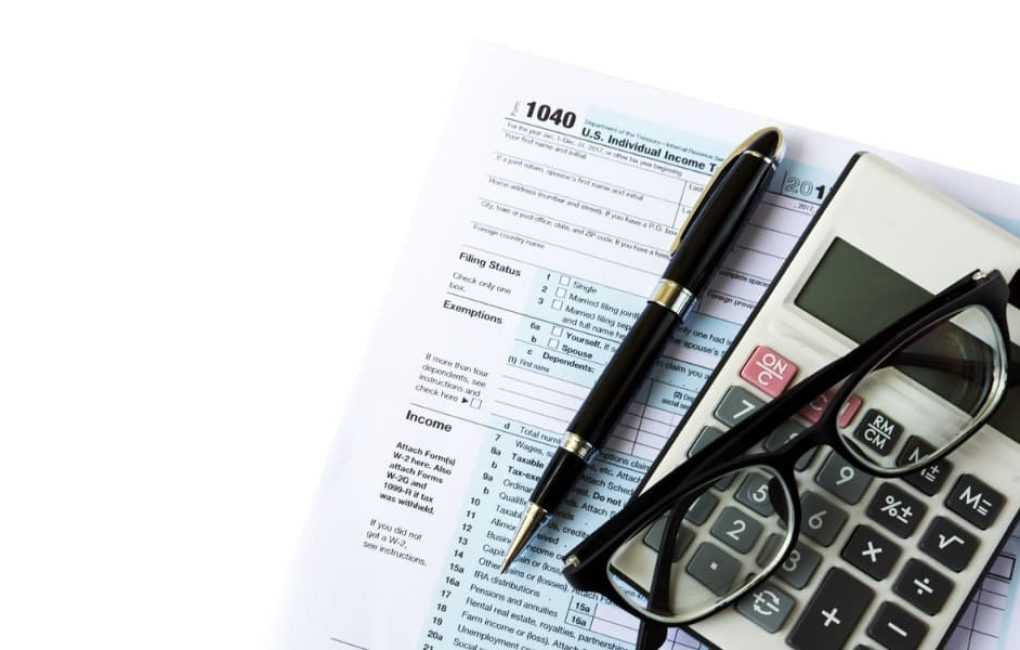 A Tax Form, Pair Of Glasses, Pen, And Calculator On A White Background, Representing The Scope Of An Audit