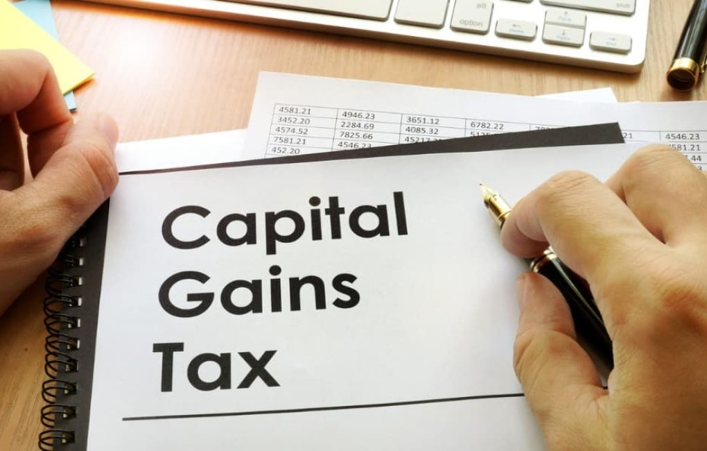 Capital Gains Tax Documents On A Desk Near A Person’s Hands